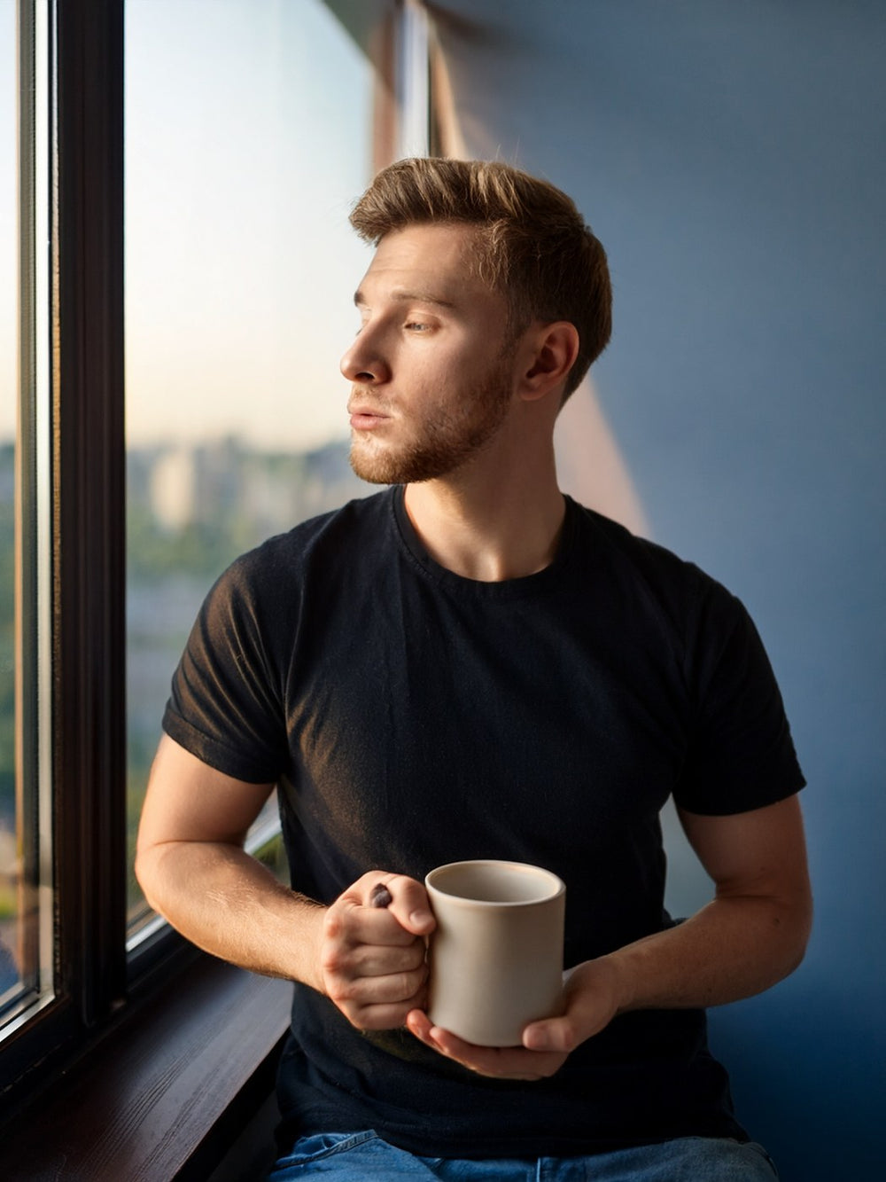 Man in a black tee by a window at dawn