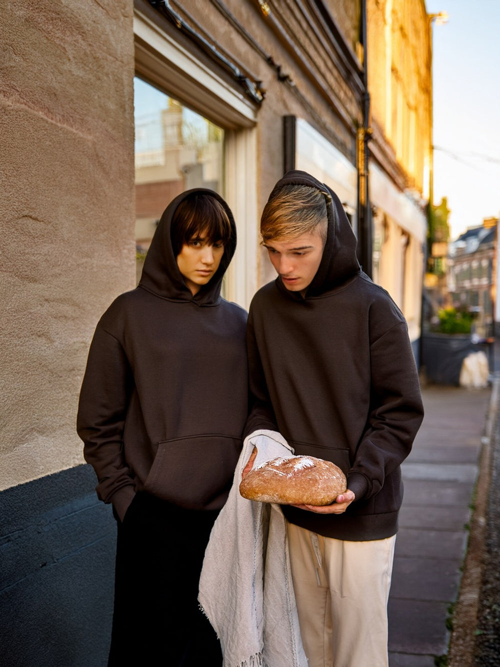 Two friends in hoodies sharing bread on a London street